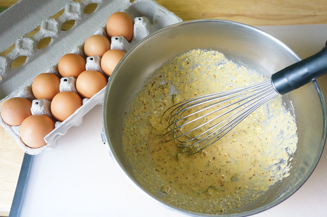Cornmeal beaten with eggs in a stainless steel bowl, with a carton of eggs in the background: the mixture is a bright, super-sunny yellow