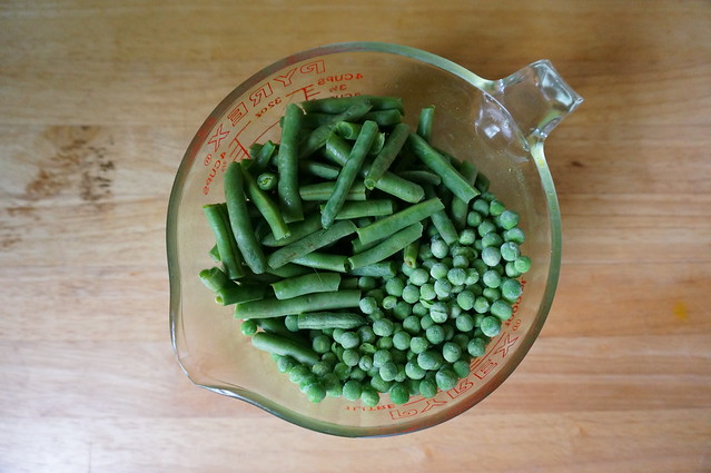Frozen peas share a measuring cup with bite-size pieces of green beans. They're divided neatly down the middle, green beans on the left, and peas on the right.