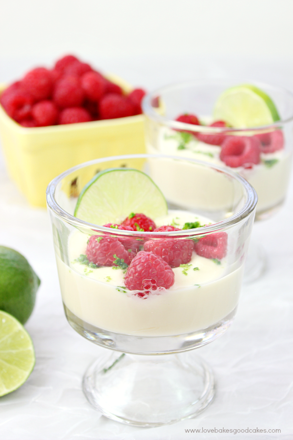 Lime Posset with Fresh Raspberries in two glasses and a bowl of fresh raspberries nearby.